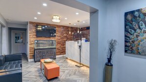 A modern lobby with a wooden wall, a reception desk, a large TV, and a peacock-themed painting.