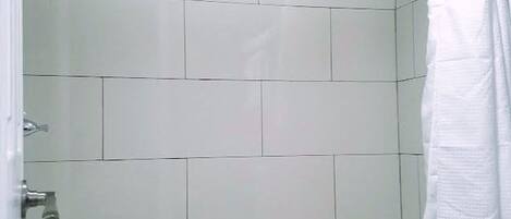 A bathroom with white tiled walls, a bathtub, and a shower curtain.