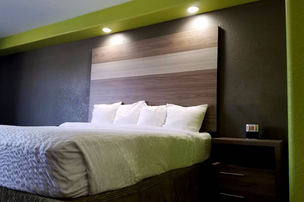A neatly made bed with white linens and pillows, a wooden headboard, and a bedside table with a clock.