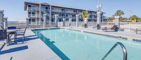 A swimming pool with a 3 FT depth marking, lounge chairs, and a building with balconies in the background.