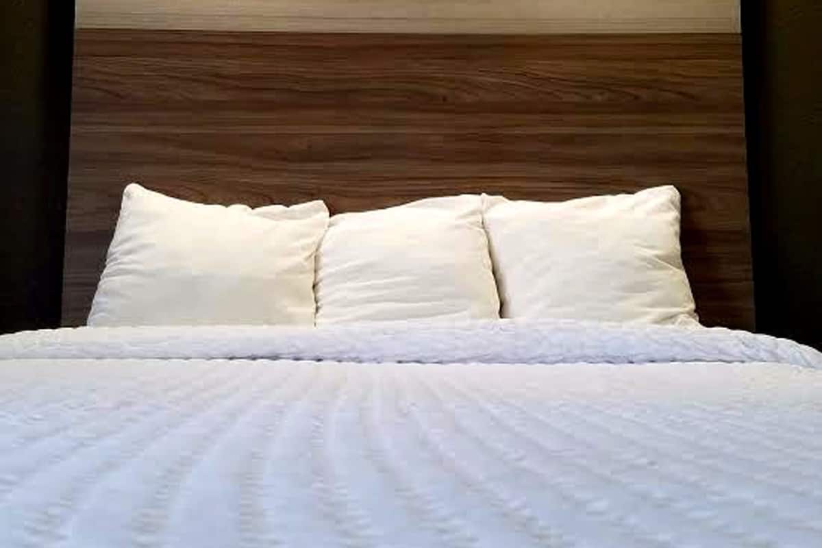 A bed with white bedding and pillows, a wooden headboard, and two ceiling lights.