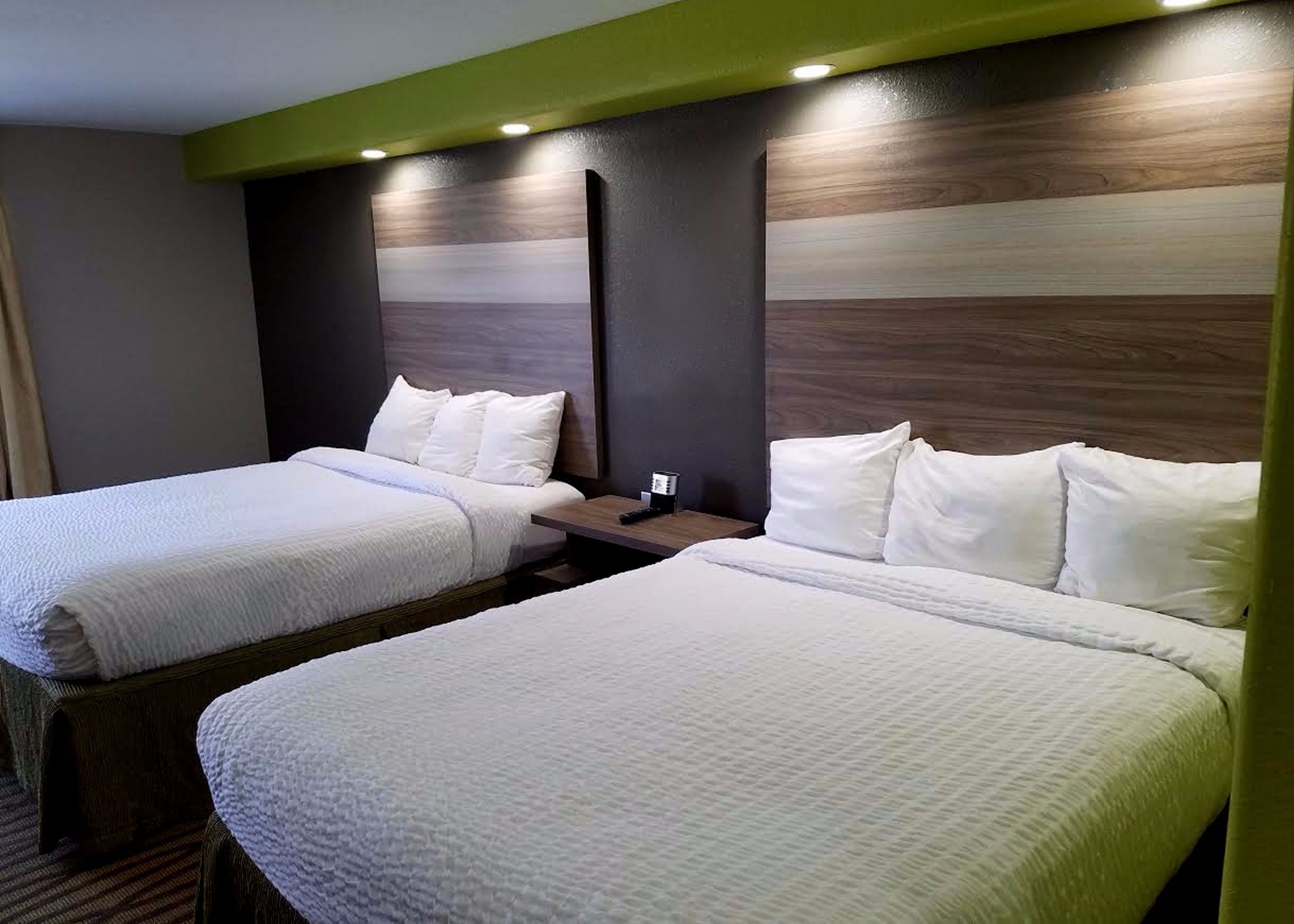 Habitación de hotel con dos camas, cada una con ropa de cama y almohadas blancas, cabeceros de madera y mesitas de noche con lámparas.