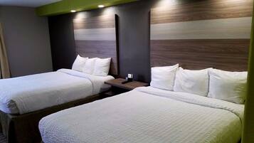 Habitación de hotel con dos camas, cada una con ropa de cama y almohadas blancas, cabeceros de madera y mesitas de noche con lámparas.