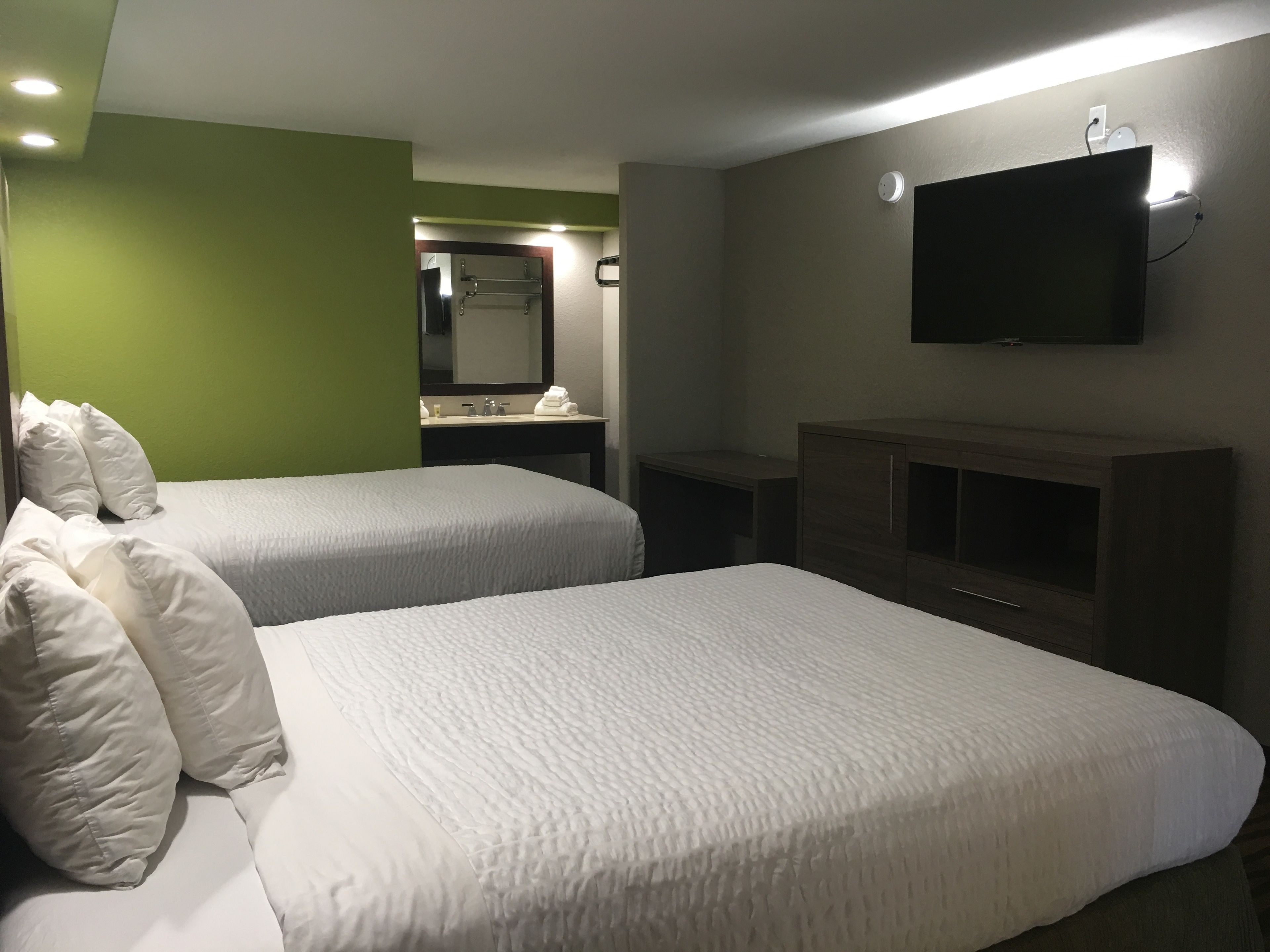 Camera d'albergo con due letti, bagno con specchio, televisore a parete e una piccola scrivania.