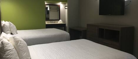 Camera d'albergo con due letti, bagno con specchio, televisore a parete e una piccola scrivania.