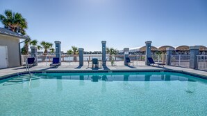 A clear swimming pool with lounge chairs and a view of the waterfront.
