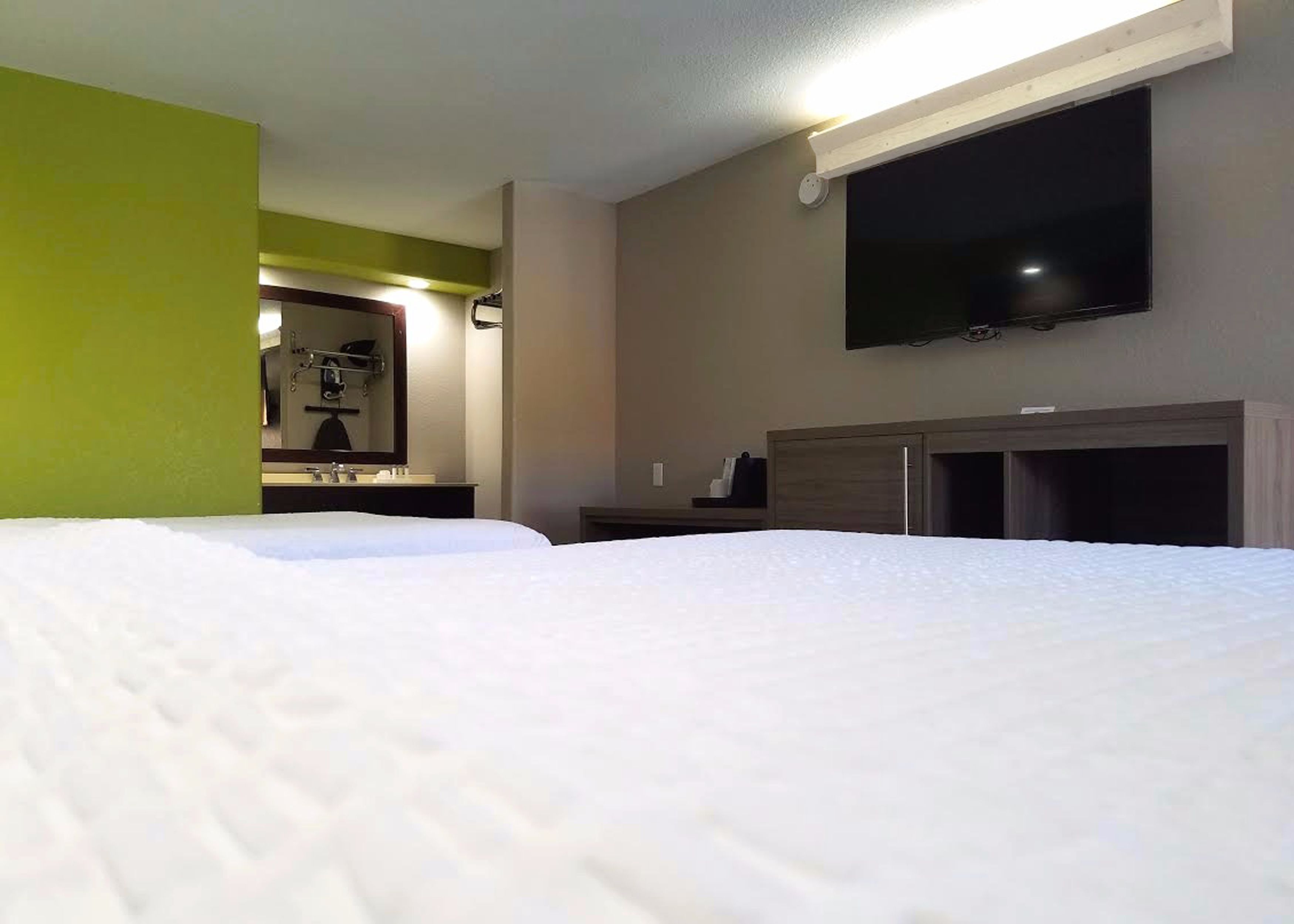 Ein Hotelzimmer mit einem großen Bett, einem an der Wand montierten Fernseher und einem Spiegel über dem Bett.