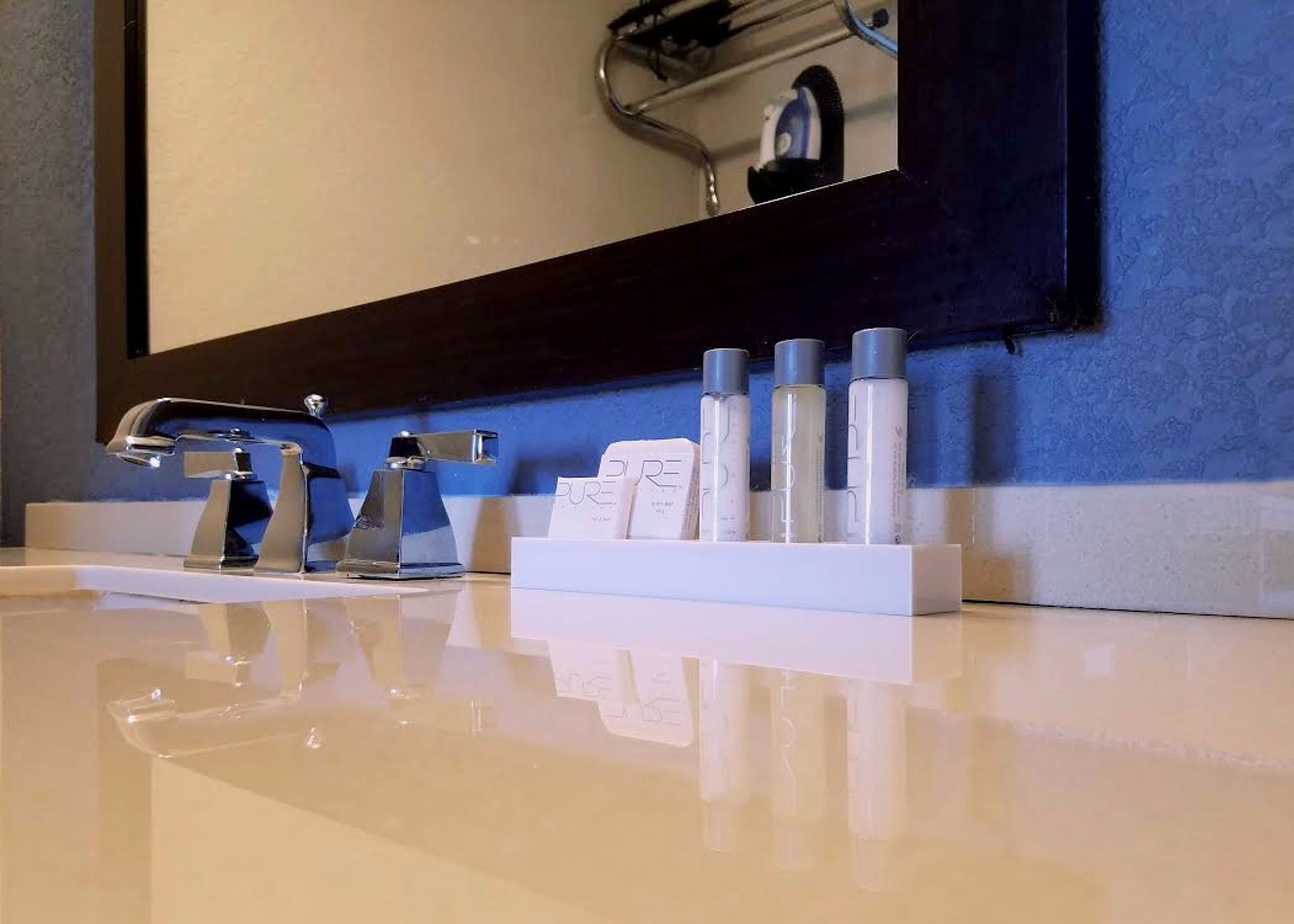 A modern bathroom with a white sink, chrome faucet, and a mirror above. There are several toiletries on the sink counter.