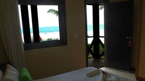 A hotel room with a bed, a window with a view of the beach, and a door leading outside. - Anaui Pousada (Ipojuca)