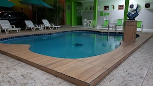 A swimming pool with a wooden deck, surrounded by lounge chairs and a green wall. - Pousada Ouriço (Ipojuca)