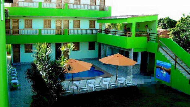 A building with a sign reading "POUSADA OURIÇO" and a pool area with lounge chairs and umbrellas. - Pousada Ouriço (Ipojuca)