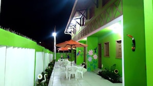 An outdoor patio area with white plastic chairs and tables, green walls, and decorative bird paintings. - Pousada Ouriço (Ipojuca)