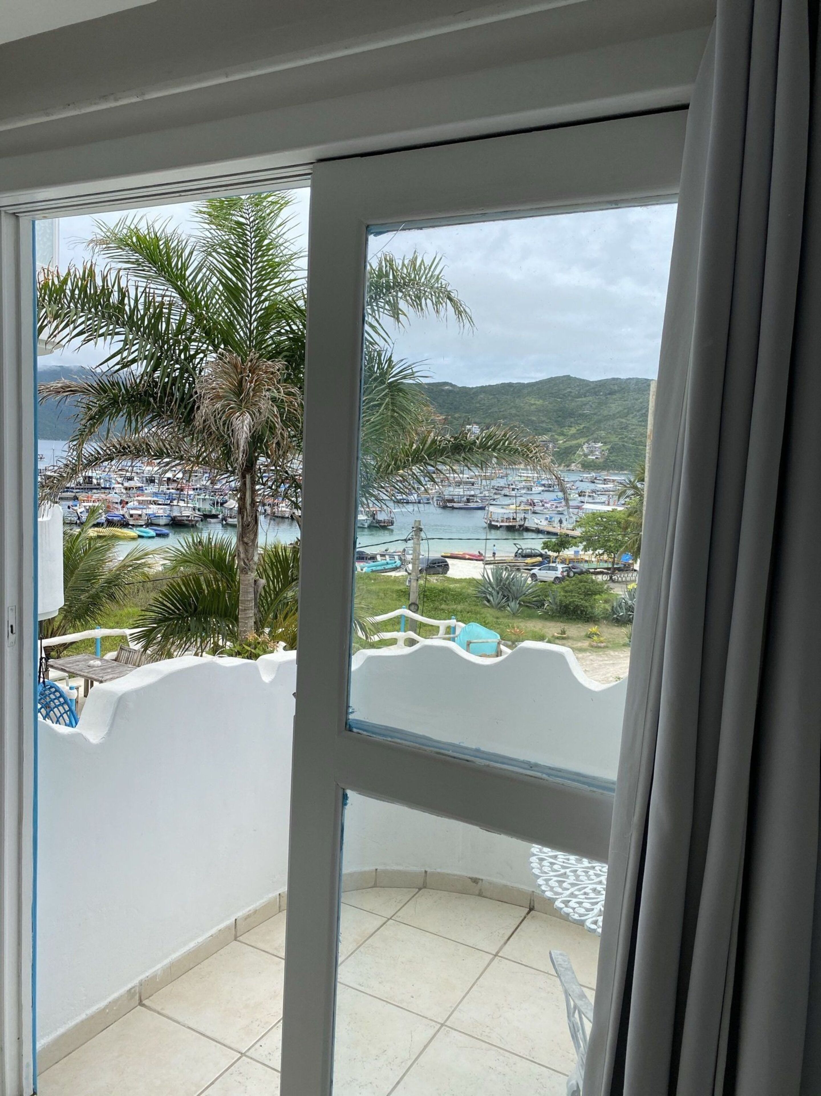 Un balcón con vistas a un puerto deportivo, palmeras y un paisaje montañoso.
