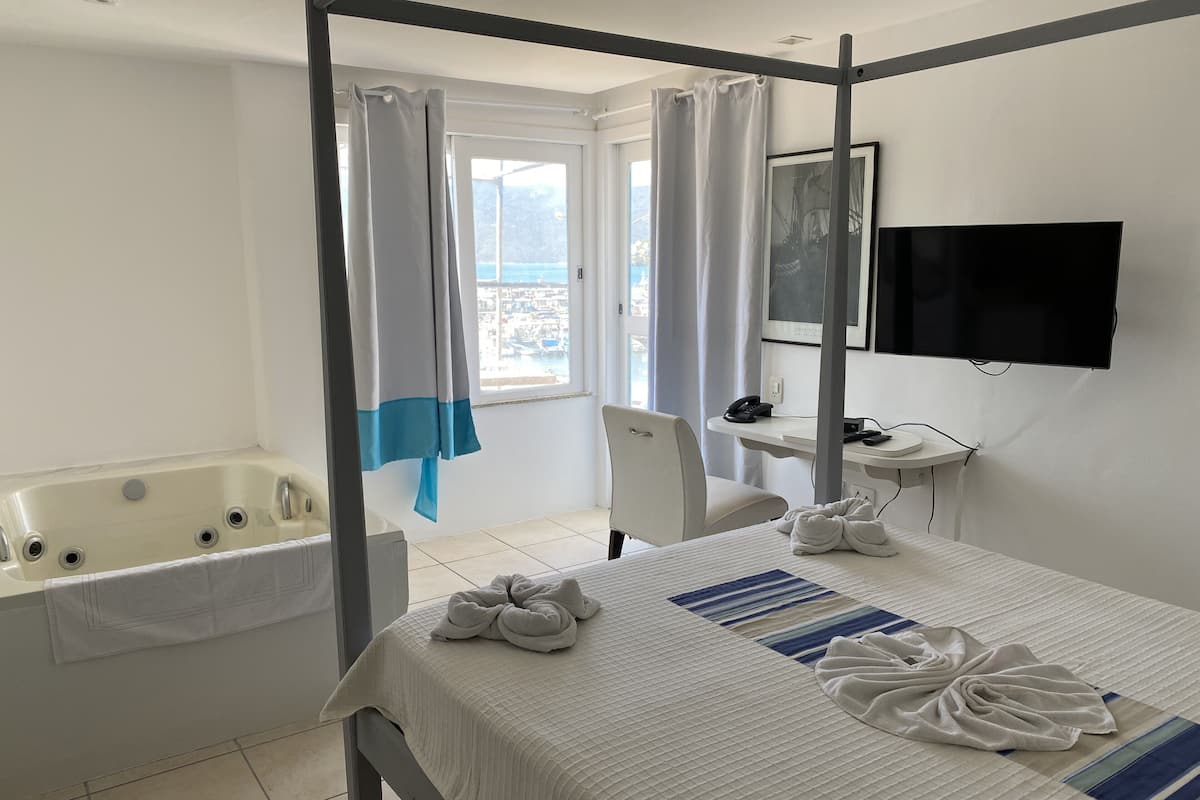 Habitació d'hotel amb un llit, un escriptori, una cadira, un televisor, una banyera i una finestra amb cortines.