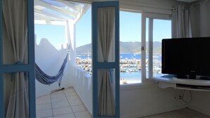 Une pièce avec un téléviseur posé sur un meuble, un hamac et une vue sur une marina et des montagnes.