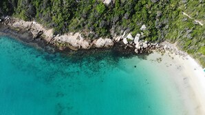 Vue aérienne d’une zone côtière caractérisée par un littoral rocheux, des eaux turquoise et limpides, et une végétation luxuriante.