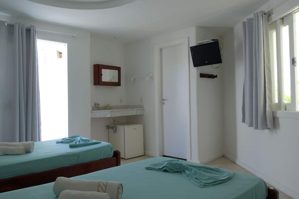 Habitació d'hotel amb dos llits, un petit vàser, un mirall, una televisió i una finestra amb cortines.