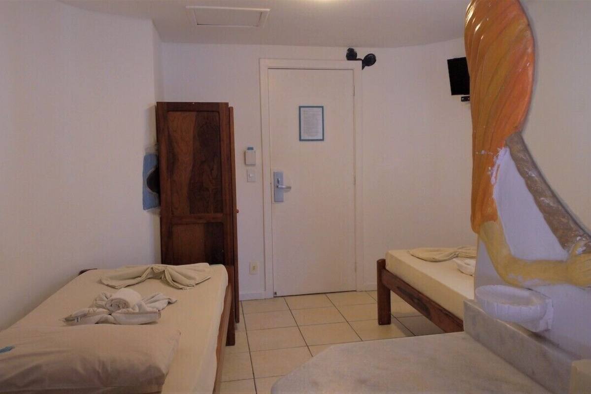 Una habitació amb dos llits individuals, un armari de fusta, una porta amb un avís i un bany amb mirall i tovallola.