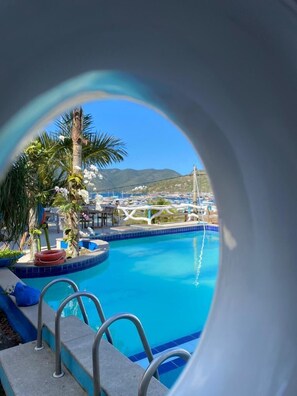 Piscina com vista para um porto de iates e montanhas ao fundo.