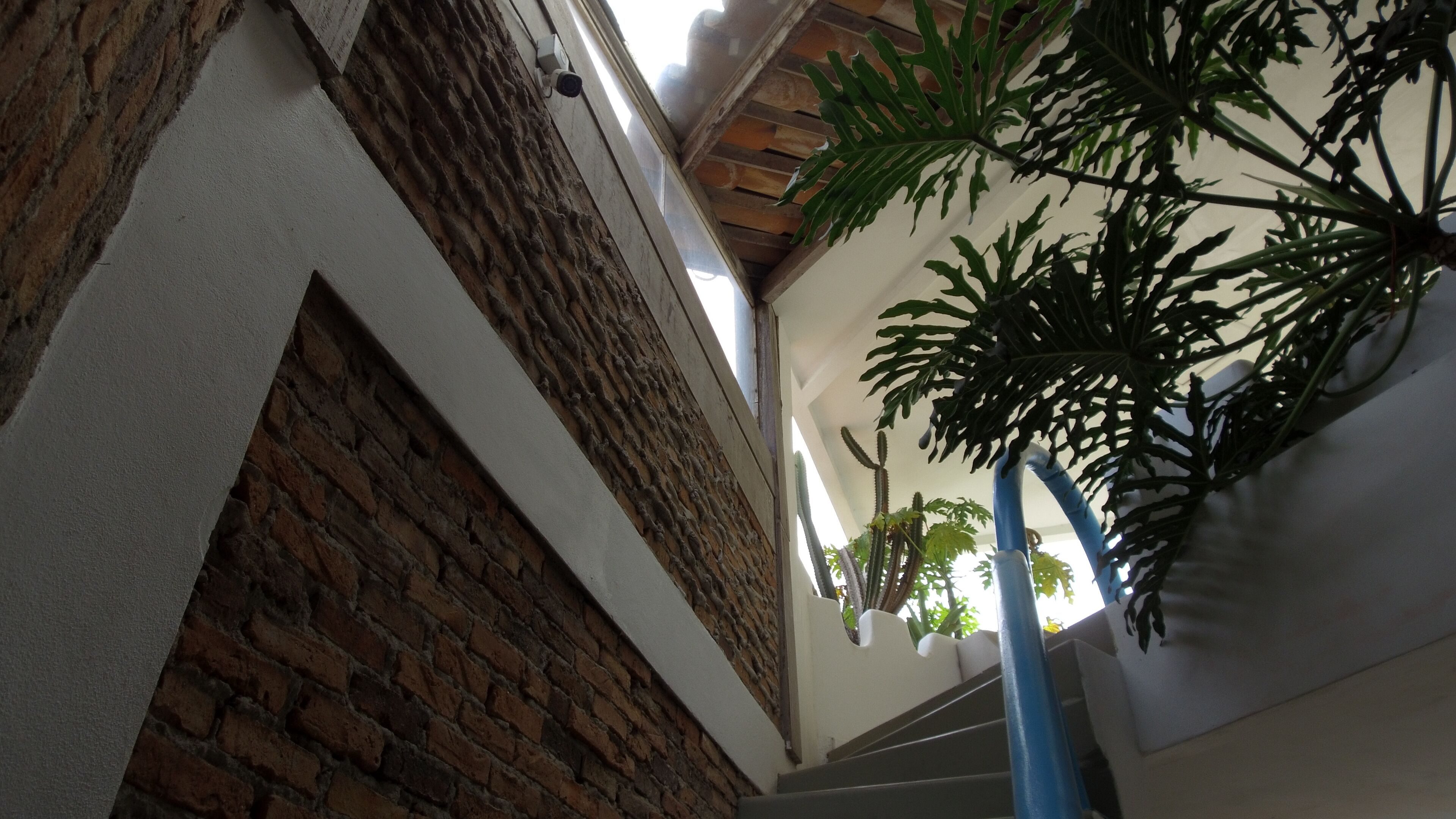 A staircase with a brick wall on one side and a white wall on the other, leading to a ceiling with a wooden beam.