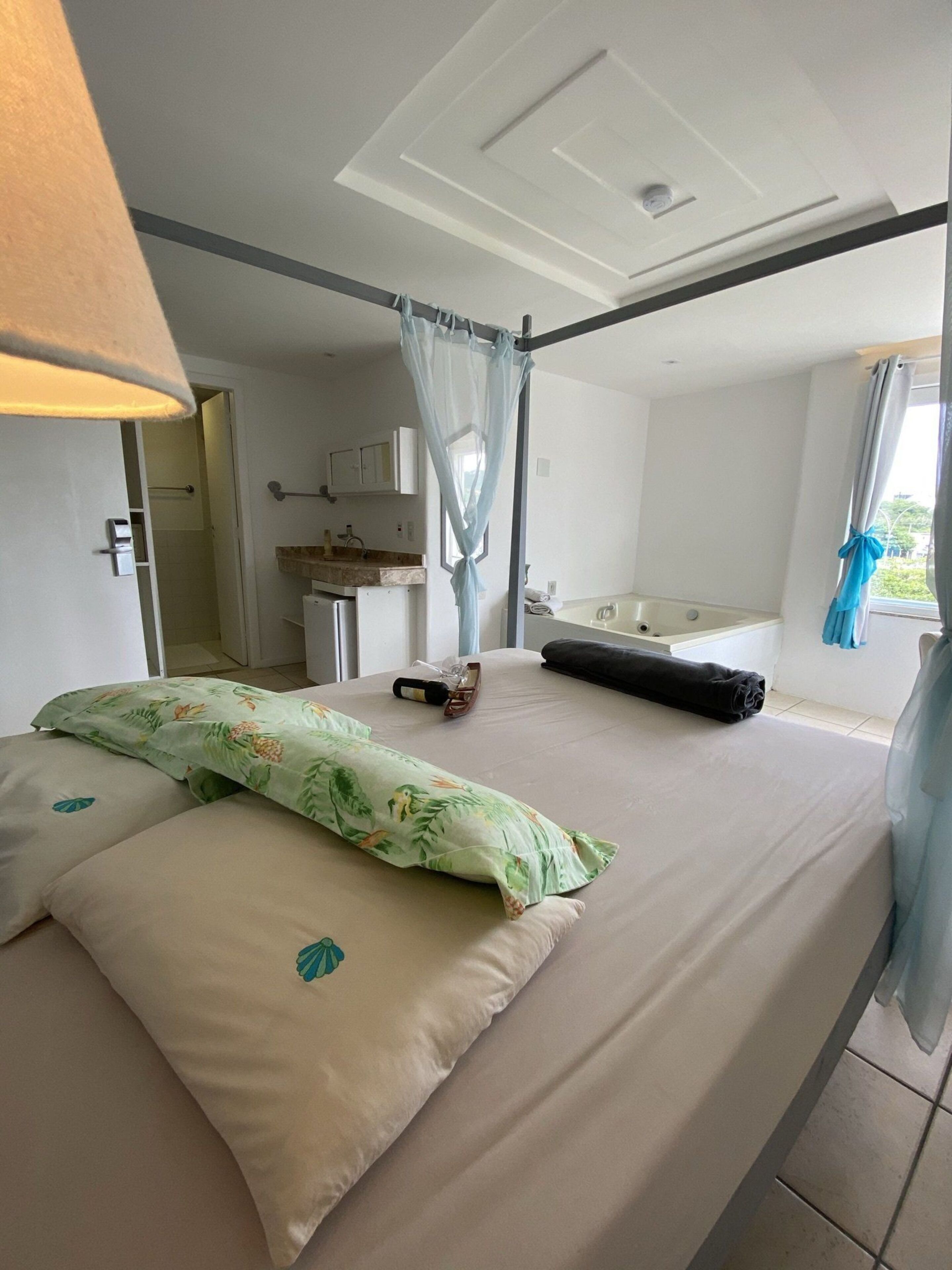 Hotelkamer met een bed, een baldakijn, een badkamer met een bad en een raam met gordijnen.