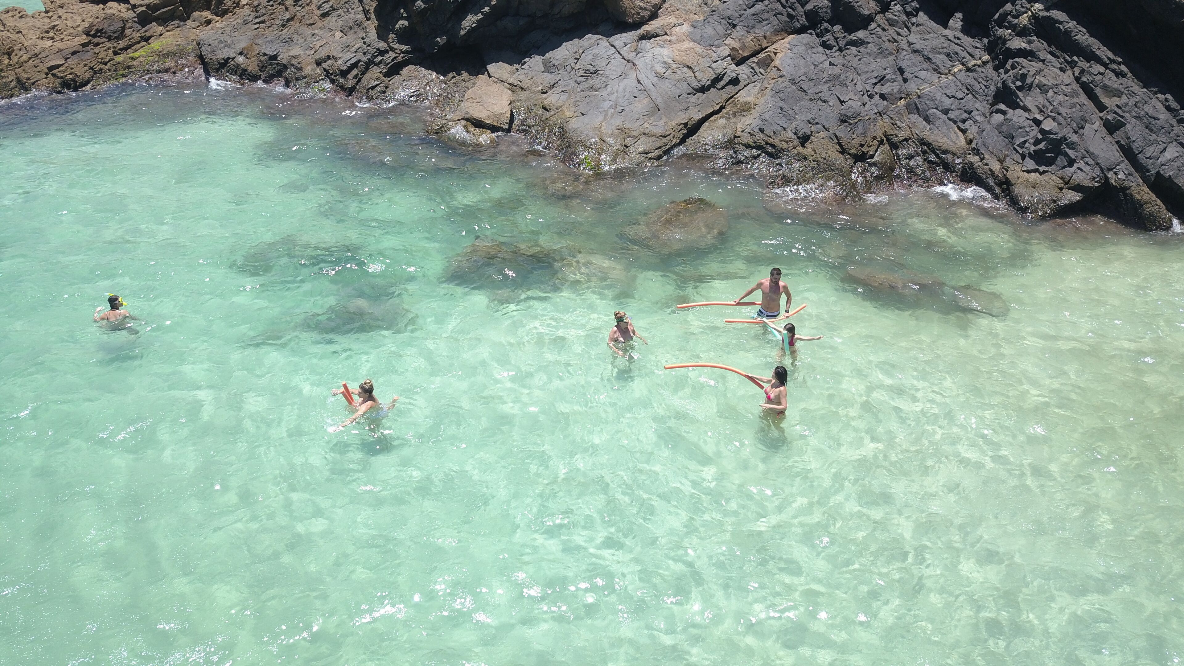 Un groupe de personnes nage dans une eau turquoise et limpide, près d'une falaise rocheuse.