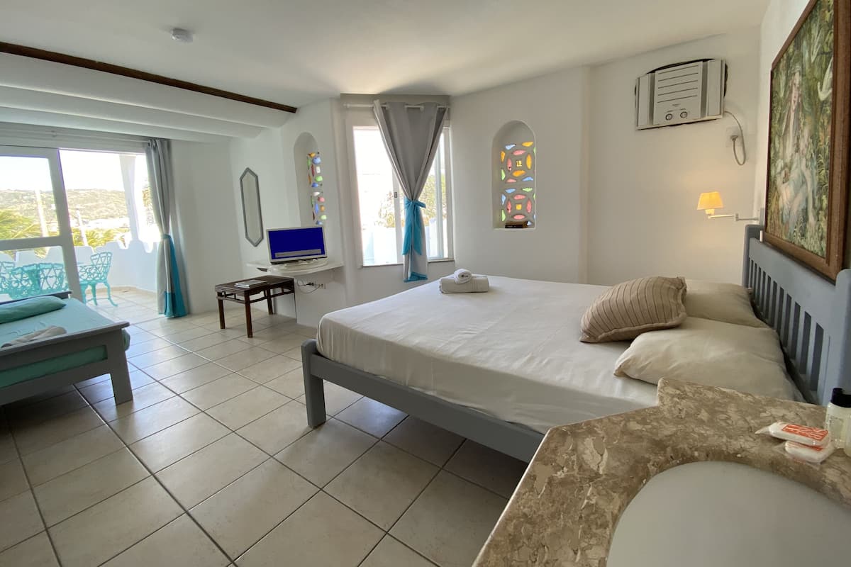 Habitació d'hotel amb llit, escriptori amb ordinador, finestra amb cortines, quadre a la paret i bany amb rentapins i mirall.