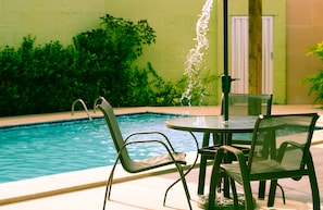 A poolside area with a table and chairs, a water feature, and lush greenery. - Pousada Angra do Porto (Ipojuca)