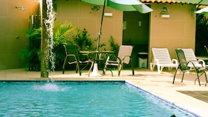 A swimming pool with a water feature, surrounded by lounge chairs and umbrellas, indicating a relaxation area.