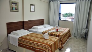 A hotel room with two beds, striped bedding, a wooden headboard, a window with curtains, and a chair. - Pousada Porto Familly (Ipojuca)