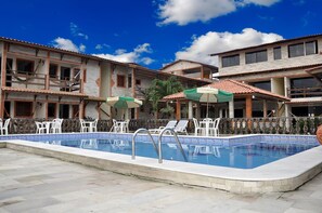 Una piscina con sillones de descanso y sombrillas, rodeada de edificios de varios pisos con balcones y ventanas.