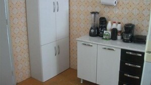 A kitchen with white cabinets, a countertop with a blender, coffee maker, and bottles. - Hostel Guerreiro (Maceió)