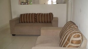 A living room with a beige sofa and a striped throw blanket. - Hostel Guerreiro (Maceió)