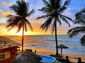A beach scene with palm trees, a swimming pool, and a house with a tiled roof.