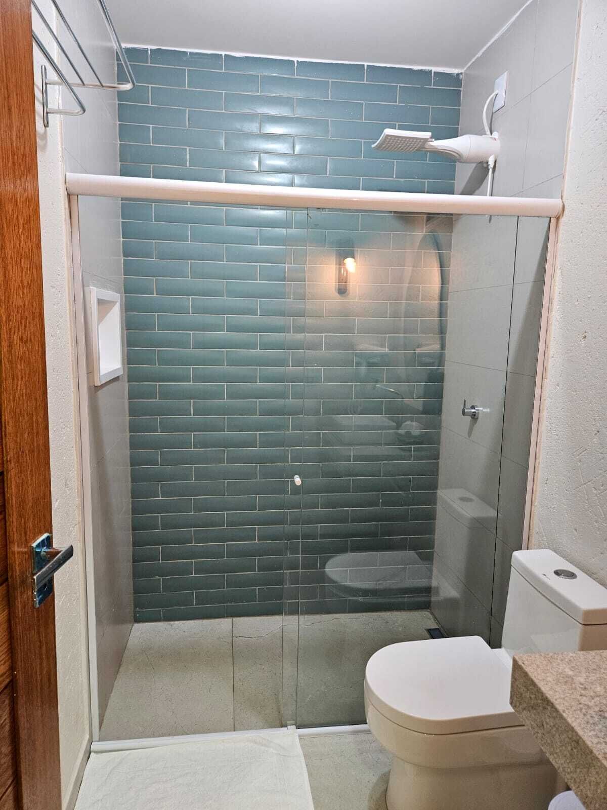 Un baño con ducha de mampara de vidrio, inodoro blanco y salpicadero de azulejos.