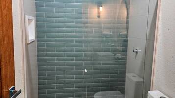 Un baño con ducha de mampara de vidrio, inodoro blanco y salpicadero de azulejos.