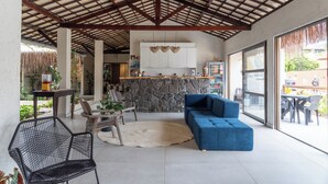 A covered patio area with a stone wall, a blue sofa, and a black chair. - Pousada Sempre Graciosa (Marechal Deodoro)