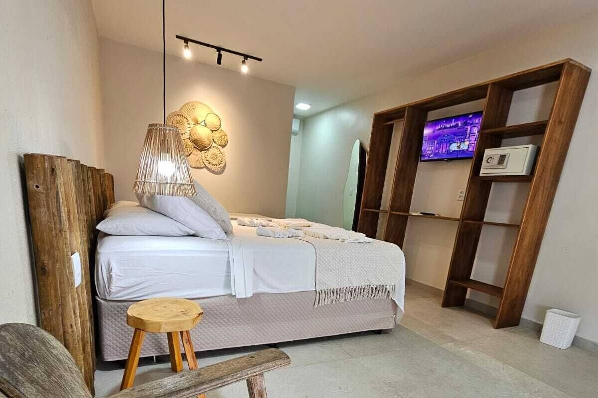 Un dormitorio moderno con una cama, un banco de madera, un taburete pequeño, una lámpara de pared y un televisor sobre una estantería.