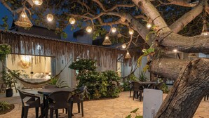 An outdoor patio area with stone flooring, black chairs, a hammock, and hanging lights. - Pousada Sempre Graciosa (Marechal Deodoro)
