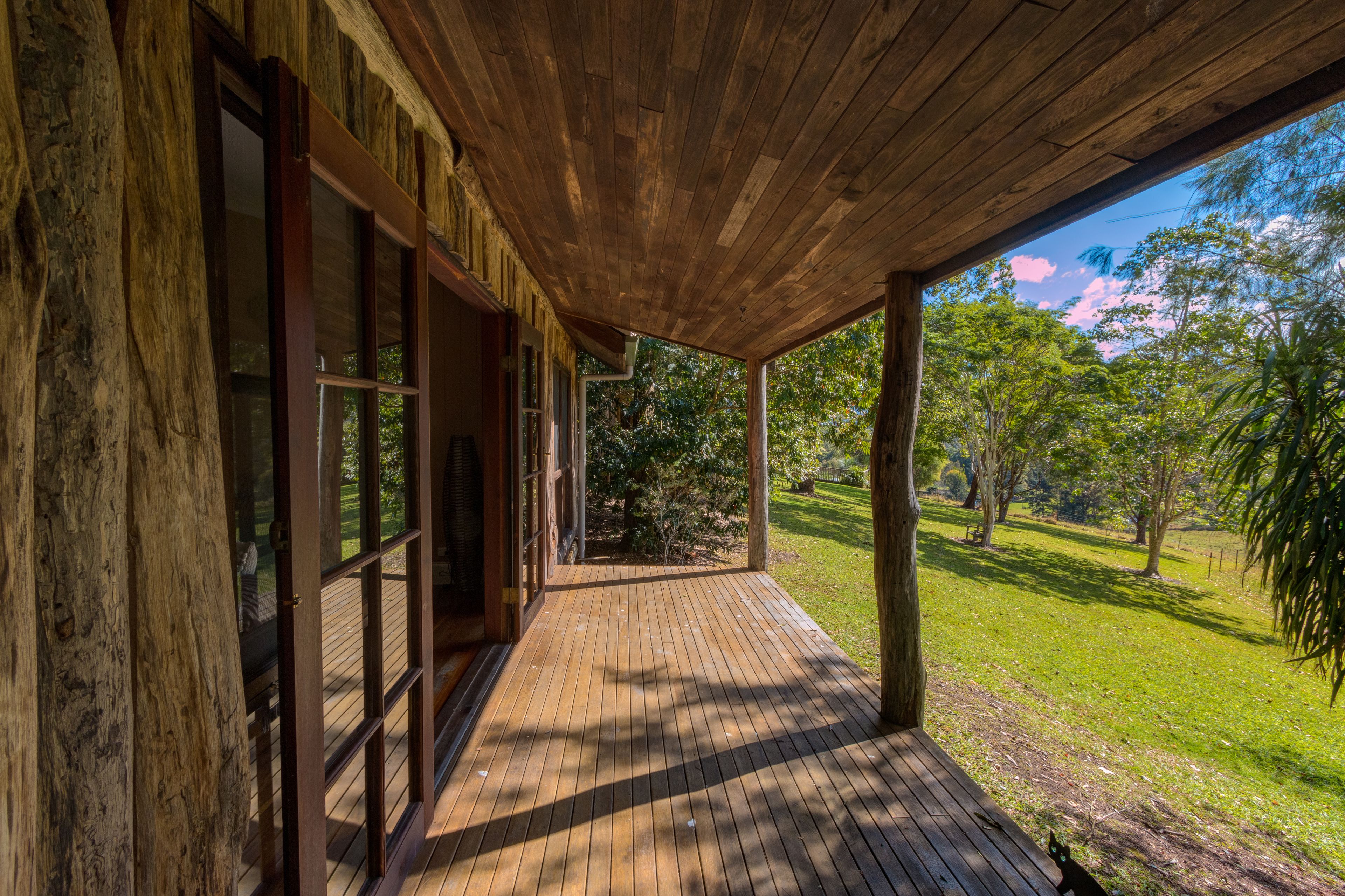 A wooden deck with large windows and a view of a grassy area with trees.