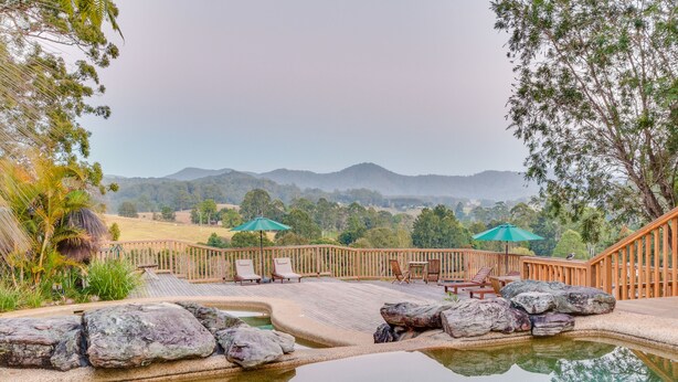 Un espace piscine doté d’une terrasse en bois, de chaises longues et offrant une vue sur les montagnes lointaines.