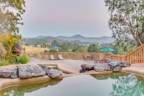 A pool area with a wooden deck, lounge chairs, and a view of distant mountains. - Friday Creek Retreat (Upper Orara)