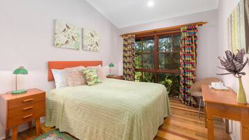 Un dormitorio con cama, mesitas de noche, escritorio, ventilador de techo y ventana con cortinas.