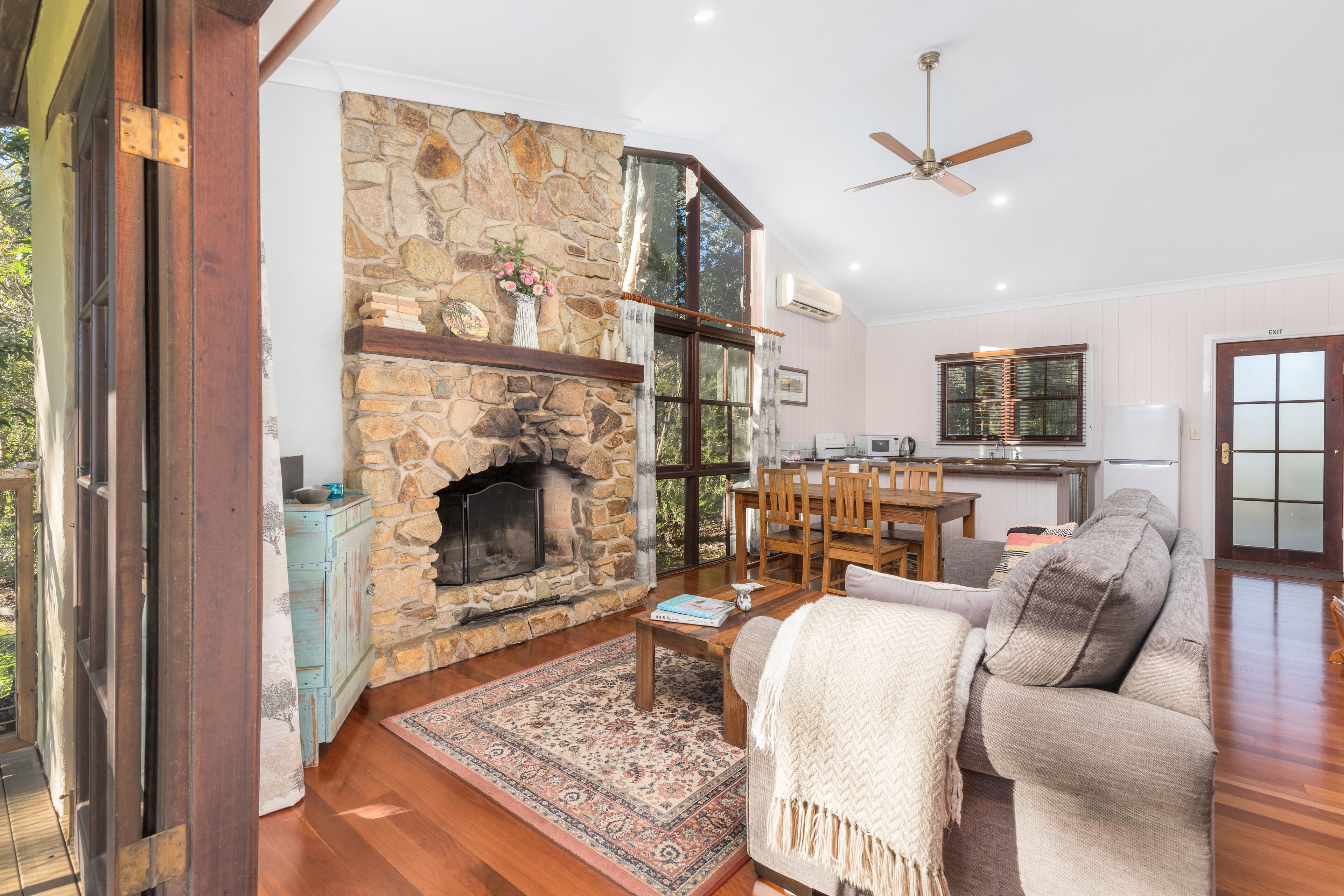 A cozy living room with a stone fireplace, wooden furniture, and a view of the outdoors.
