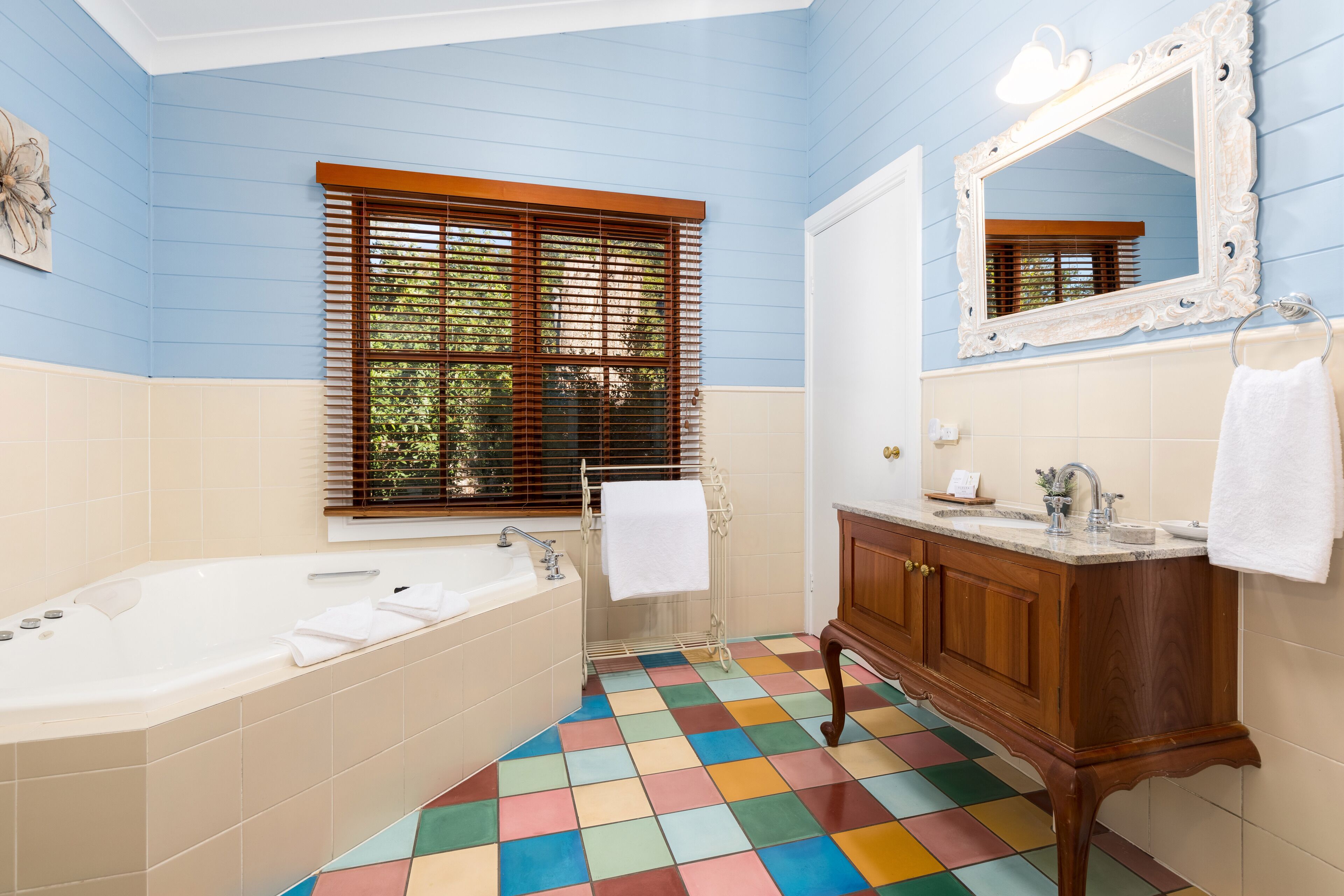 Un baño con una bañera grande, un tocador de madera, un espejo y una ventana con persianas.