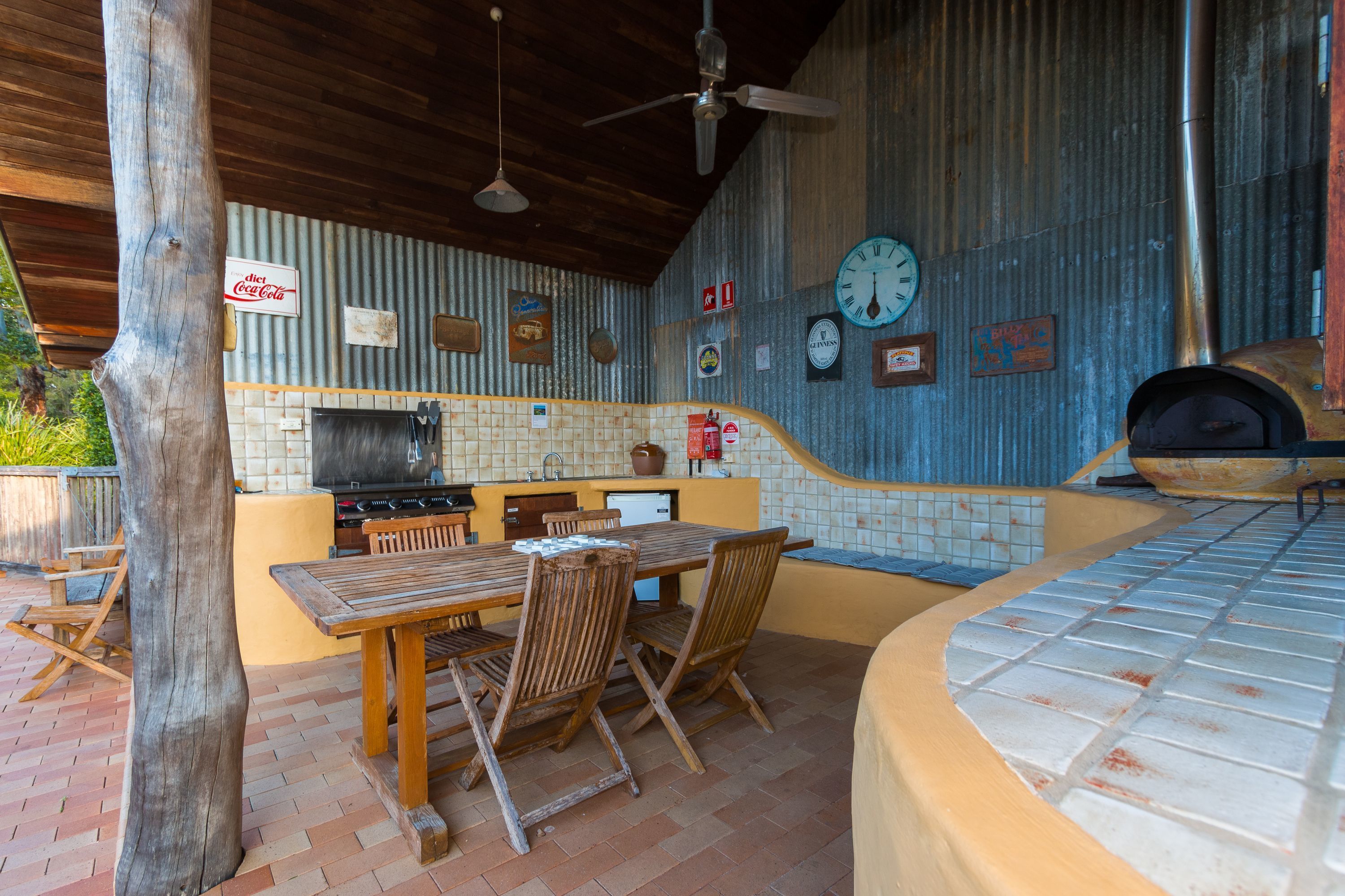 An outdoor kitchen area with a wooden table and chairs, a grill, and a pizza oven.