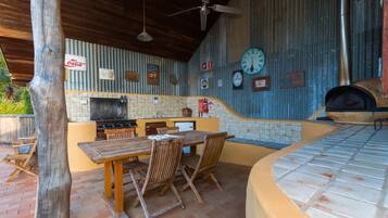 An outdoor kitchen area with a wooden table and chairs, a grill, and a pizza oven.