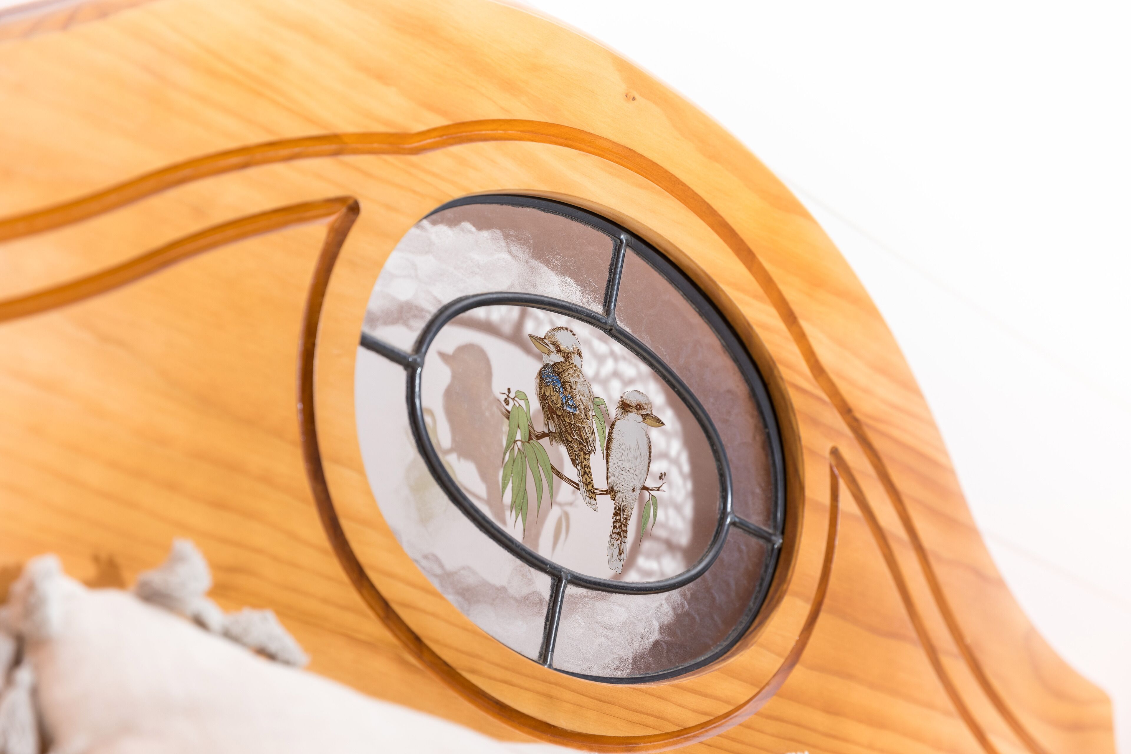 Un objet en bois doté d’une fenêtre circulaire représentant deux oiseaux perchés sur des branches.