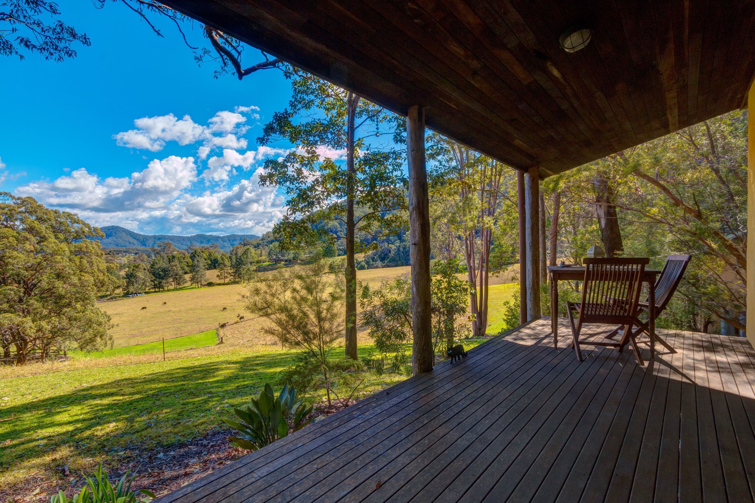 Una terraza de madera con una mesa y sillas que da a un campo de césped y colinas boscosas.
