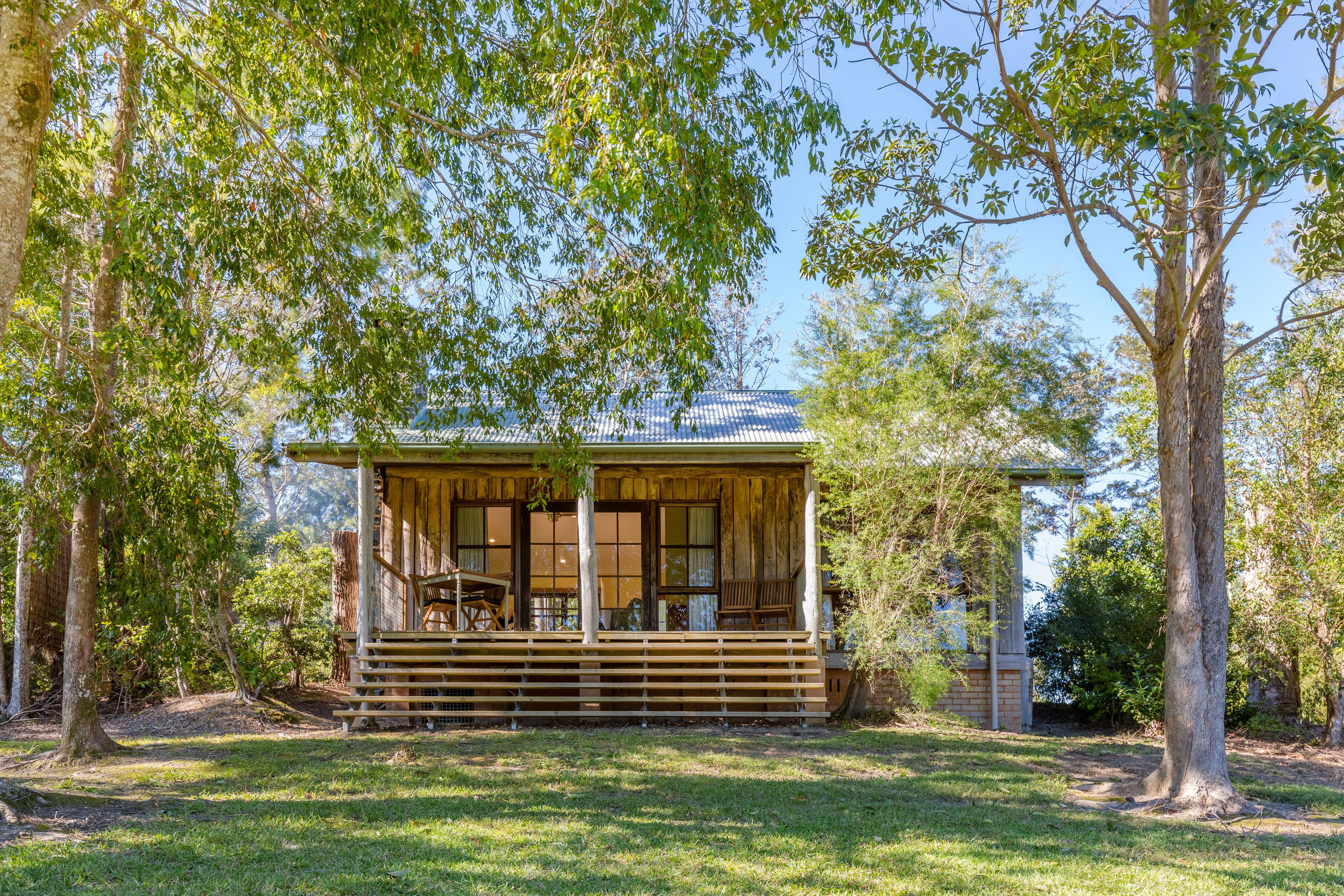 A wooden cabin with a porch, surrounded by trees.